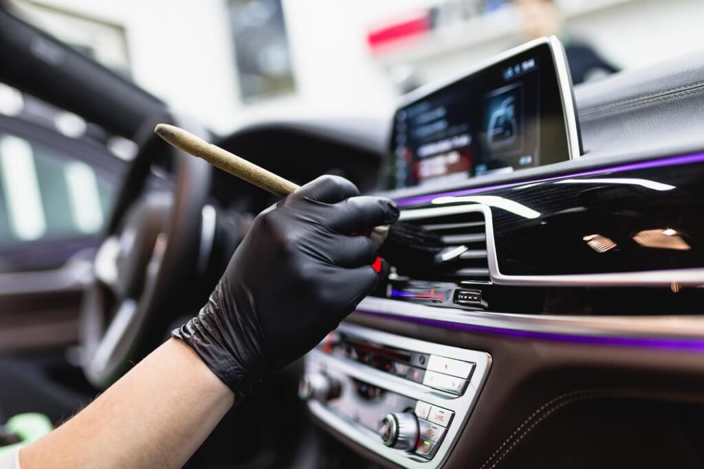 A close-up shot captures a person's hand meticulously washing a red car using a white cloth and soapy water, showcasing the care and attention to detail involved in automotive cleaning. The action is dynamic and highlights the sparkling finish of the car.