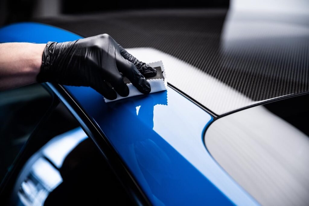 A close-up shot captures a person's hand meticulously washing a red car using a white cloth and soapy water, showcasing the care and attention to detail involved in automotive cleaning. The action is dynamic and highlights the sparkling finish of the car.